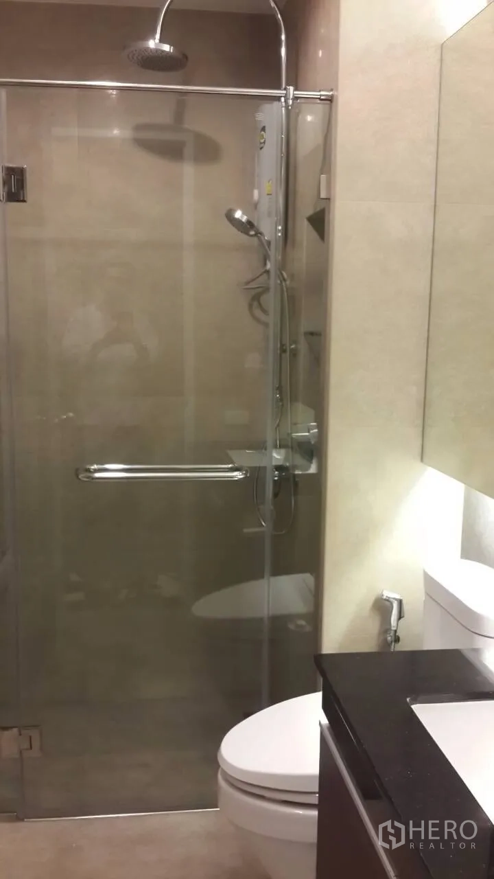 Condominium for rent in Mueang Samut Prakan, Samut Prakan - Sleek bathroom with glass-enclosed rain shower, handheld sprayer, modern vanity, and toilet.