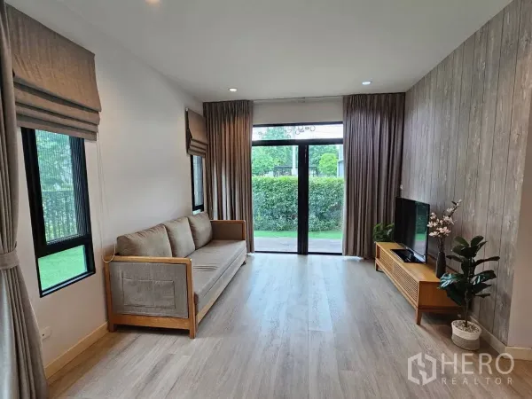 Detached House for rent or sale in Don Mueang, Bangkok - Long living area with TV, sofa, and floor-to-ceiling windows opening to the patio.