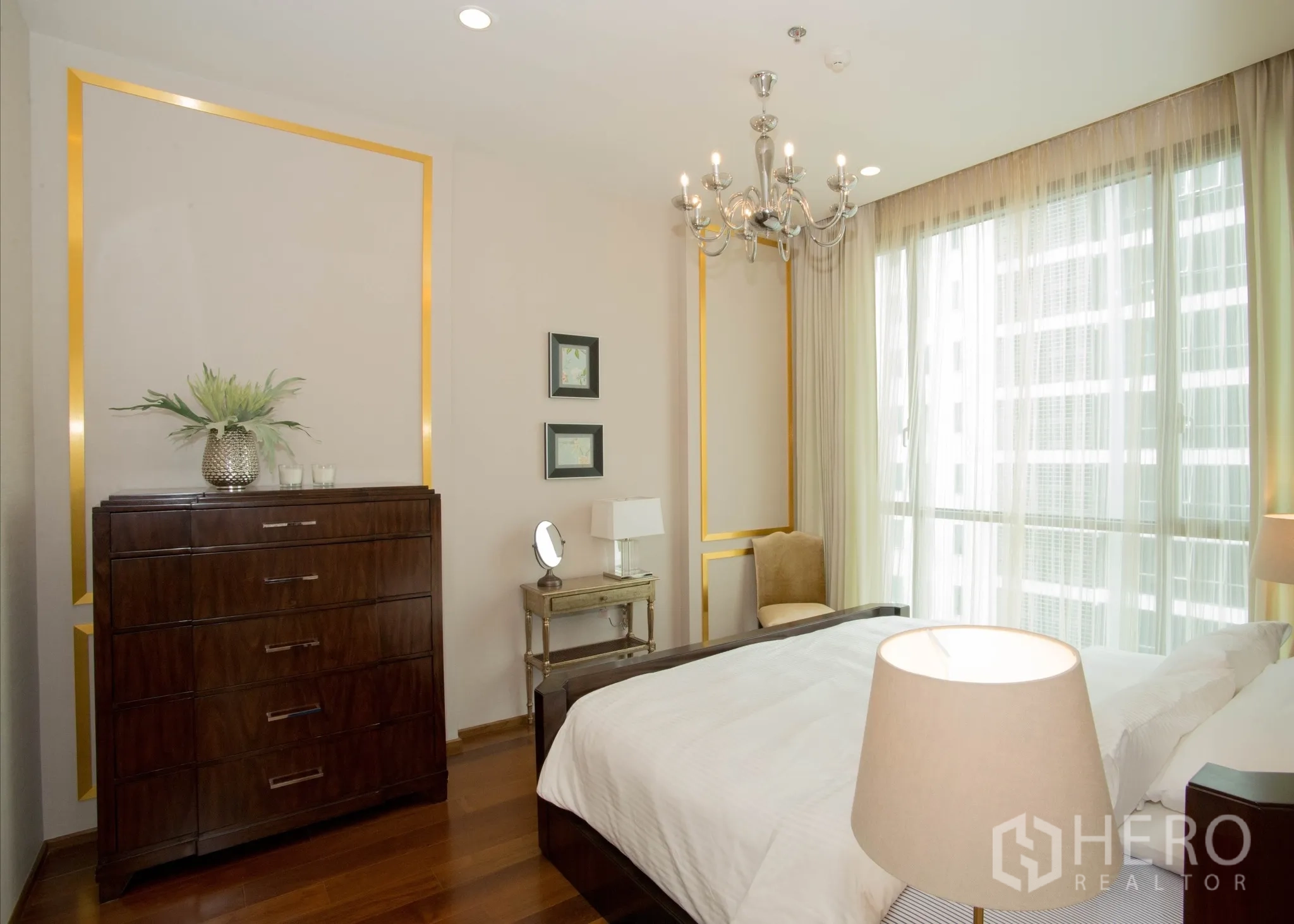 Condominium for rent in Watthana, Bangkok - Bedroom angle showing tall dresser, chandelier lighting, and large windows with a city outlook.