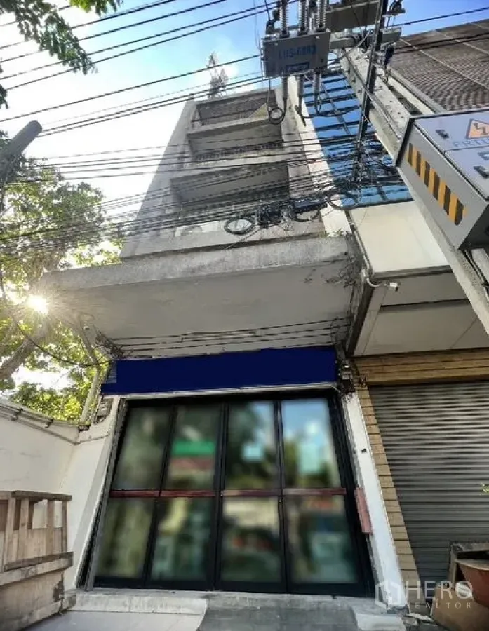 店屋 出租在Watthana, Bangkok - 多层商铺外立面，玻璃门面配蓝色遮阳篷，素坤逸支路上，临近BTS通罗站（瓦他那，曼谷）。