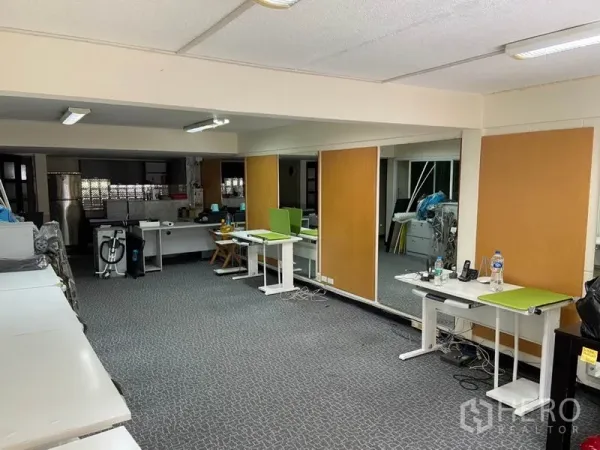 Townhouse for rent in Khlong Toei, Bangkok - Spacious open-plan room with carpet flooring, desks, fluorescent lighting, and mirrored wall partitions.