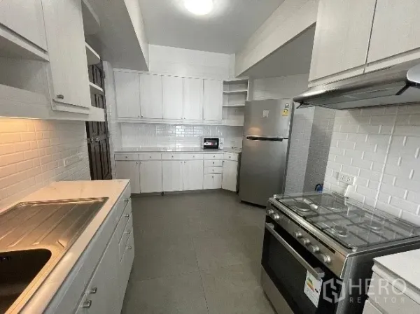 公寓 出租在Khlong Toei, Bangkok - 明亮的封闭式厨房，白色橱柜、地铁砖墙、不锈钢冰箱与燃气灶，曼谷公寓内景