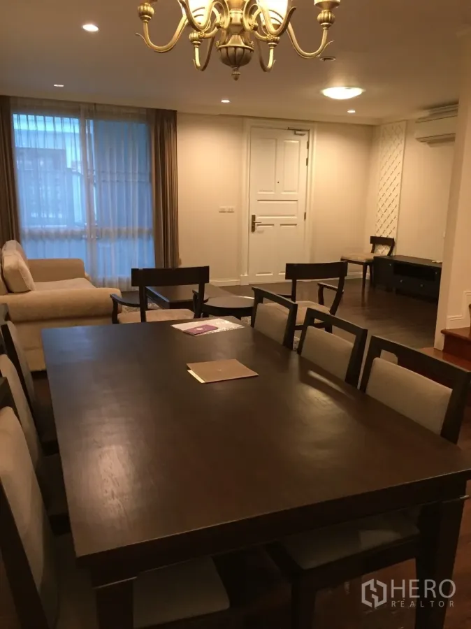 คอนโด ขายในHuai Khwang, Bangkok - พื้นที่รับประทานอาหารและนั่งเล่นโทนอบอุ่น โต๊ะไม้สีเข้ม โคมแชนเดอเลียร์ โซฟา และผ้าม่านโปร่งในคอนโด 2 ห้องนอน กรุงเทพฯ