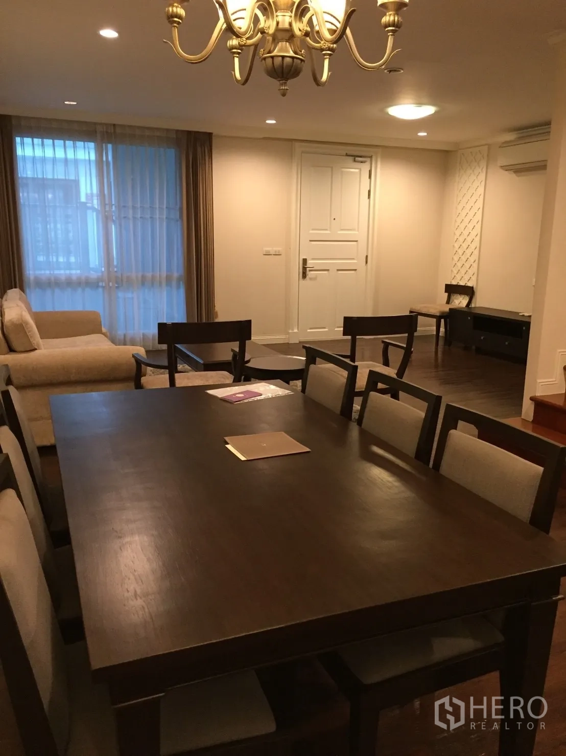คอนโด ขายในHuai Khwang, Bangkok - พื้นที่รับประทานอาหารและนั่งเล่นโทนอบอุ่น โต๊ะไม้สีเข้ม โคมแชนเดอเลียร์ โซฟา และผ้าม่านโปร่งในคอนโด 2 ห้องนอน กรุงเทพฯ