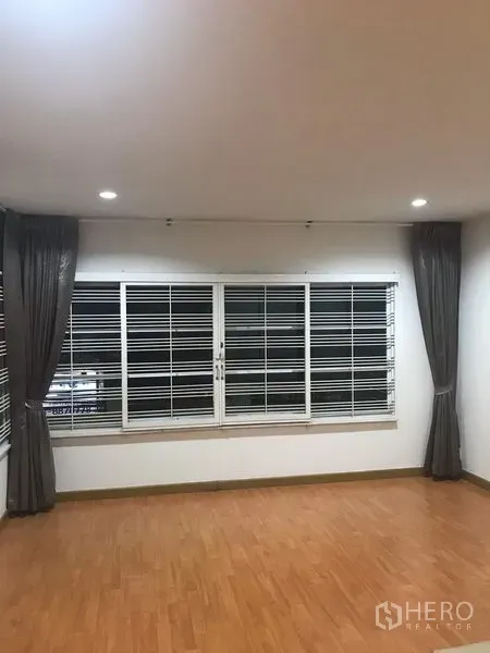 Detached House for rent in Din Daeng, Bangkok - Bright room with large windows, security grilles, dark curtains and wood-look flooring.