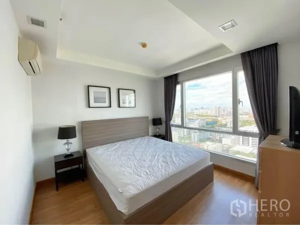 Condominium for rent in Huai Khwang, Bangkok - Master bedroom with large windows and wide city skyline view.