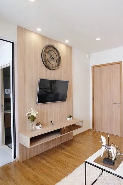 Condominium for sale in Watthana, Bangkok - TV feature wall with wood paneling, floating console and decorative clock.