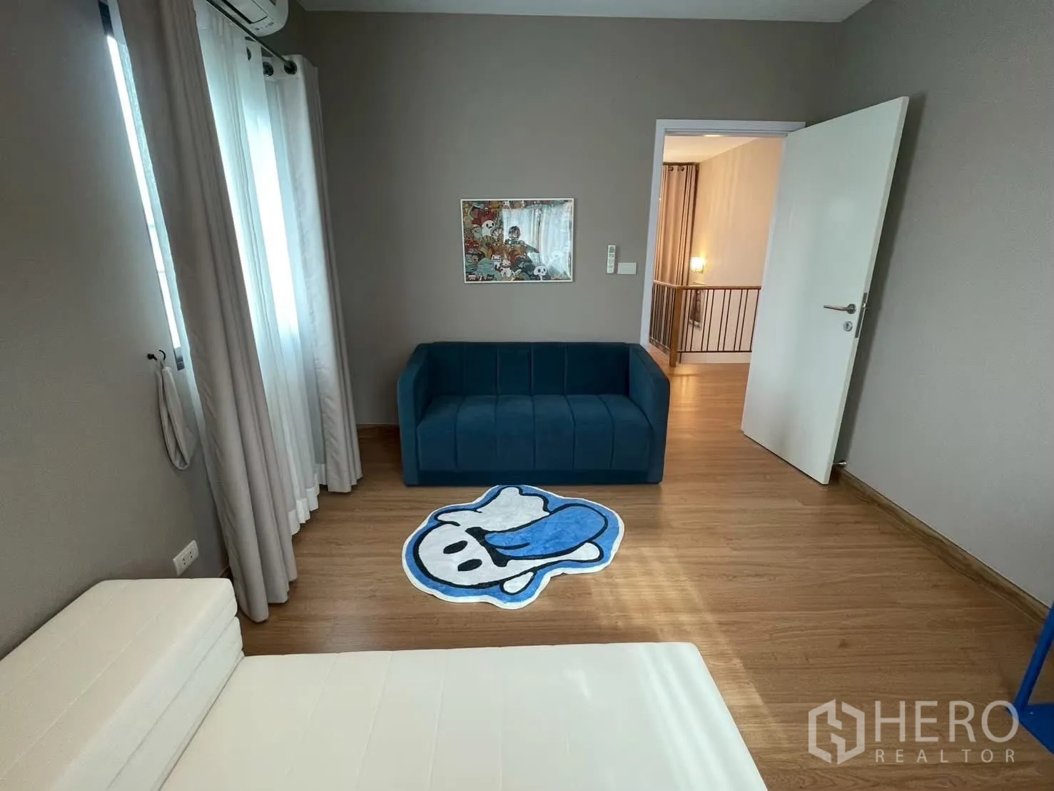 Detached House for rent in Bang Phli, Samut Prakan - Cozy room with a navy sofa, cartoon rug, sheer curtains and wood flooring.