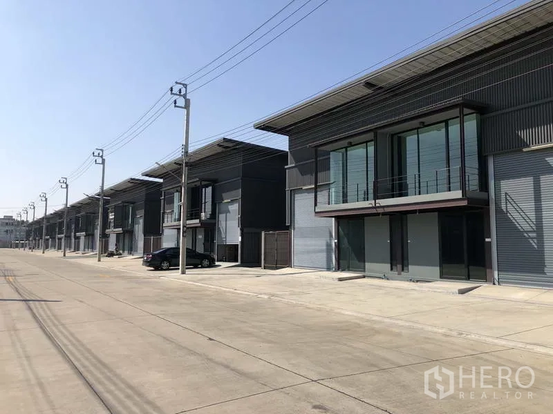 货栈 出租在Bang Phli, Samut Prakan - 沿宽阔园区道路排列的新仓库，设停车位和电线杆。