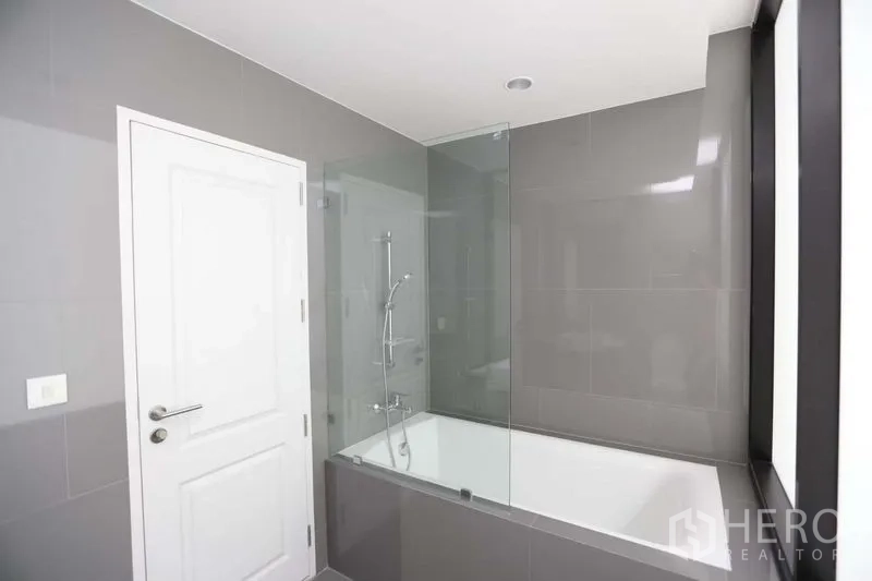 Condominium for sale in Bang Rak, Bangkok - Close-up of bathtub with glass screen and handheld shower set.