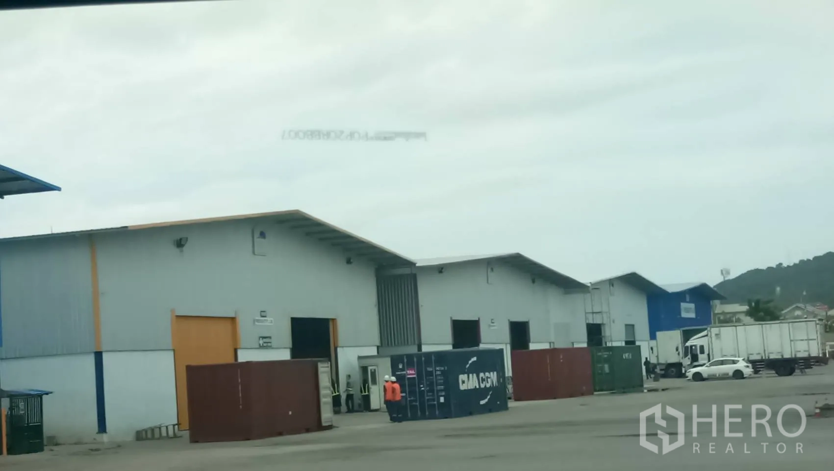 货栈 出租在Si Racha, Chon Buri - 成排灰色仓库，前方有集装箱与卡车停靠的宽阔堆场