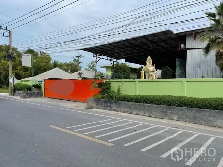 货栈 出售在Lam Luk Ka, Pathum Thani - 临街仓库入口，绿色围墙与橙色大门，内有钢结构屋顶建筑。