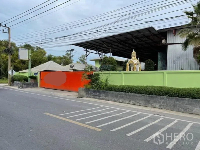 货栈 出售在Lam Luk Ka, Pathum Thani - 临街仓库入口，绿色围墙与橙色大门，内有钢结构屋顶建筑。
