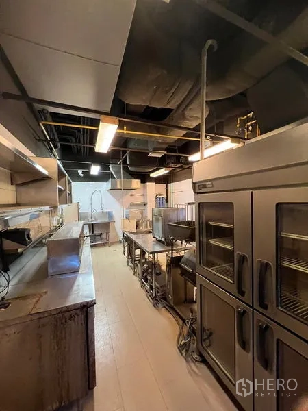 พื้นที่ขายปลีก ให้เช่า - ครัวเชิงพาณิชย์ทางยาว โต๊ะเตรียมอาหารสแตนเลส เตาอบ และท่อดูดควัน.