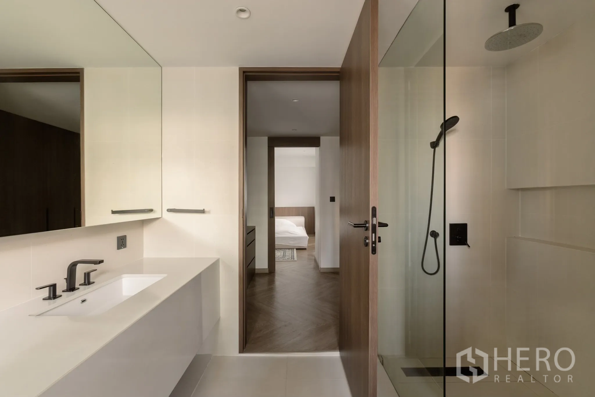 Condominium for sale in Khlong Toei, Bangkok - Contemporary bathroom with glass shower, rain showerhead and wide vanity looking toward the bedroom.