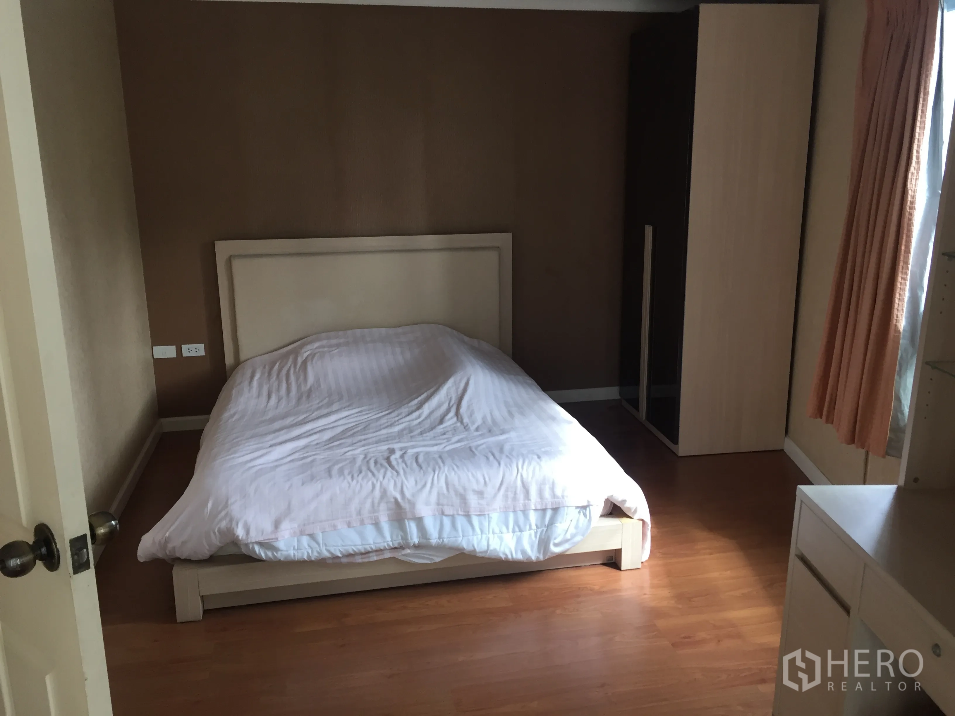 Condominium for rent in Watthana, Bangkok - Cozy bedroom with double bed, wardrobe and curtained window, warm-toned walls and wooden floor.