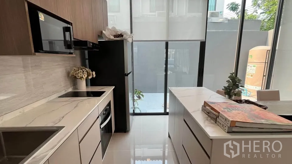 Townhouse for rent or sale in Bang Phli, Samut Prakan - Sitting area with sofa next to compact kitchen and washing machine.