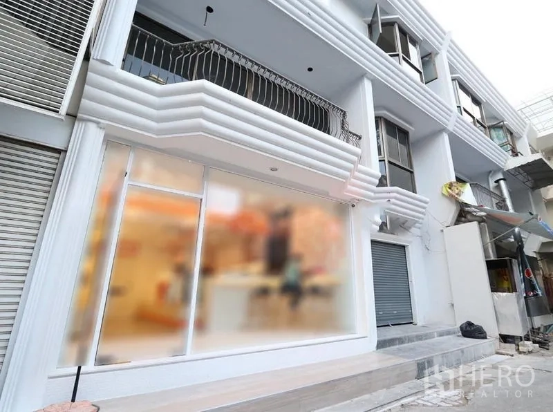 零售空间 出租在Pathum Wan, Bangkok - 现代白色临街店面，整面玻璃橱窗，带阳台与卷帘门的多层建筑外立面