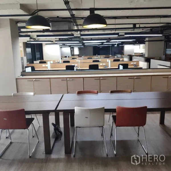 办公空间 出租 - 开放式办公区，成排工位与吊灯，前方为休闲长桌。