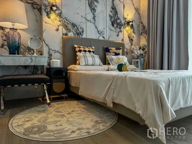 คอนโด ให้เช่า - ห้องนอนหลัก เตียงบุผ้า โต๊ะหัวเตียง และผนังลายหินอ่อนโดดเด่น