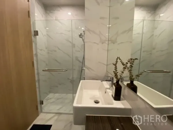 Condominium for rent in Watthana, Bangkok - Contemporary bathroom with marble-effect tiles, glass-enclosed shower and rectangular basin with large mirror.