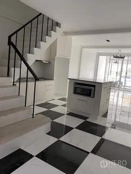 Townhouse for sale in Khlong Toei, Bangkok - Bright open-plan kitchen with island, built-in oven, black-and-white checkered floor, and a staircase.