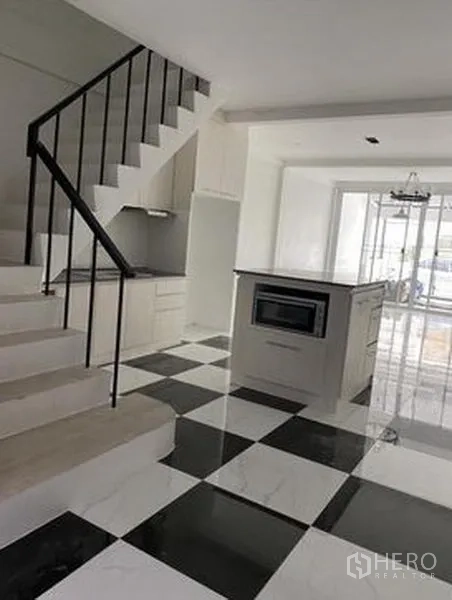 Townhouse for sale in Khlong Toei, Bangkok - Bright open-plan kitchen with island, built-in oven, black-and-white checkered floor, and a staircase.