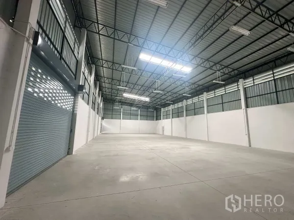 Factory for rent in Bang Len, Nakhon Pathom - Spacious production hall with high steel truss roof, skylights and a roller shutter door.