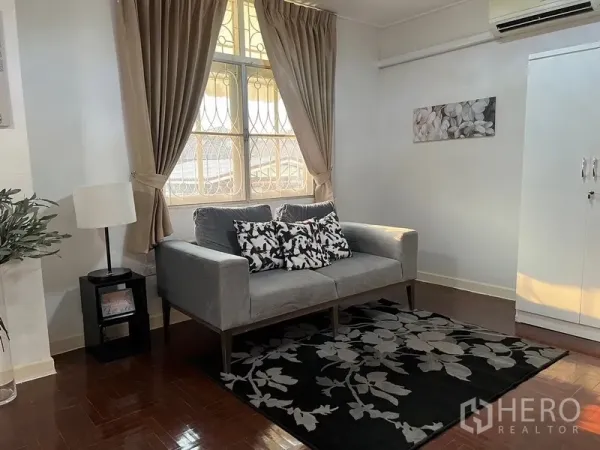 Home Office for rent in Suan Luang, Bangkok - Cozy sitting area with gray sofa, patterned rug and window drapes.