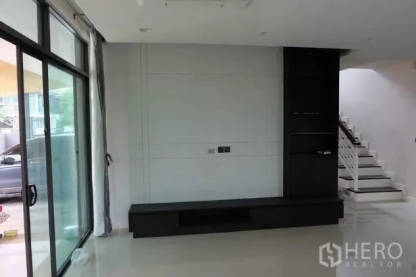 Detached House for rent in Bang Kapi, Bangkok - Living room with floor-to-ceiling sliding doors, built-in TV console and staircase to the upper floor.