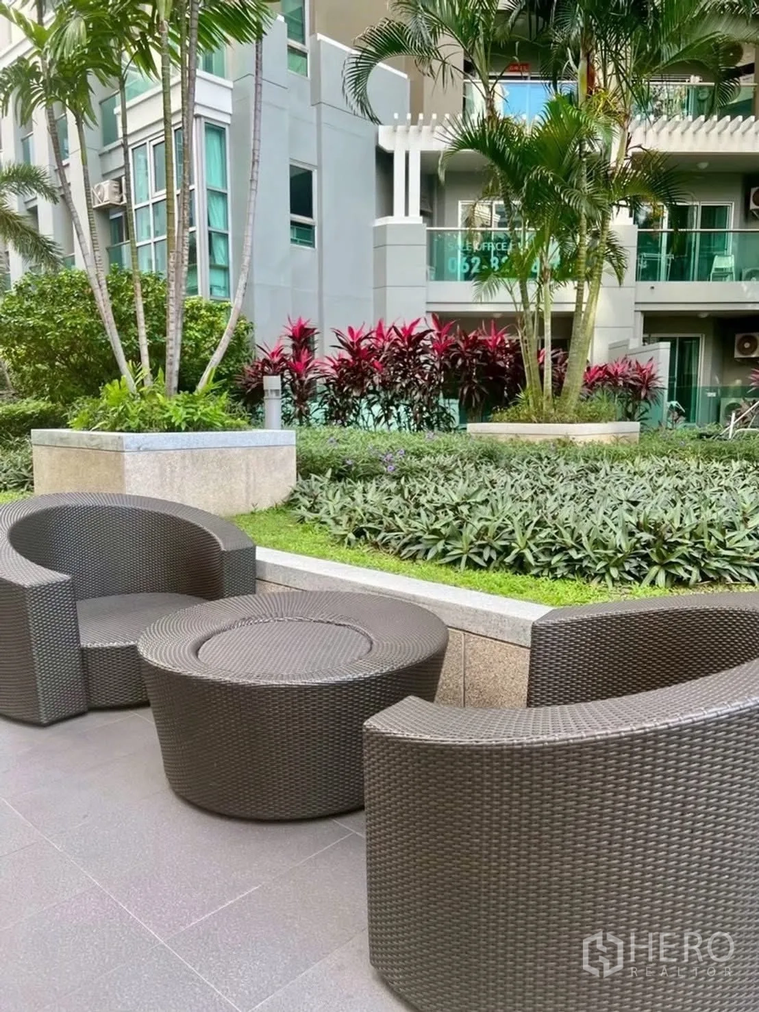 Condominium for rent in Huai Khwang, Bangkok - Outdoor garden seating area with rattan chairs beside landscaping.