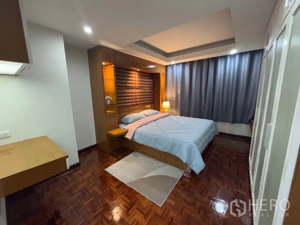 Condominium for rent in Huai Khwang, Bangkok - Primary bedroom with large bed, built-in headboard shelving, tray ceiling and blackout curtains.