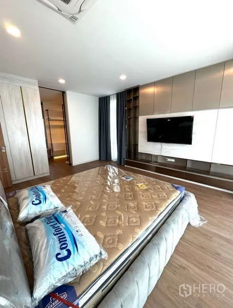 Detached House for rent in Samut Prakan - Master suite with TV wall, storage cabinetry and wood floors.
