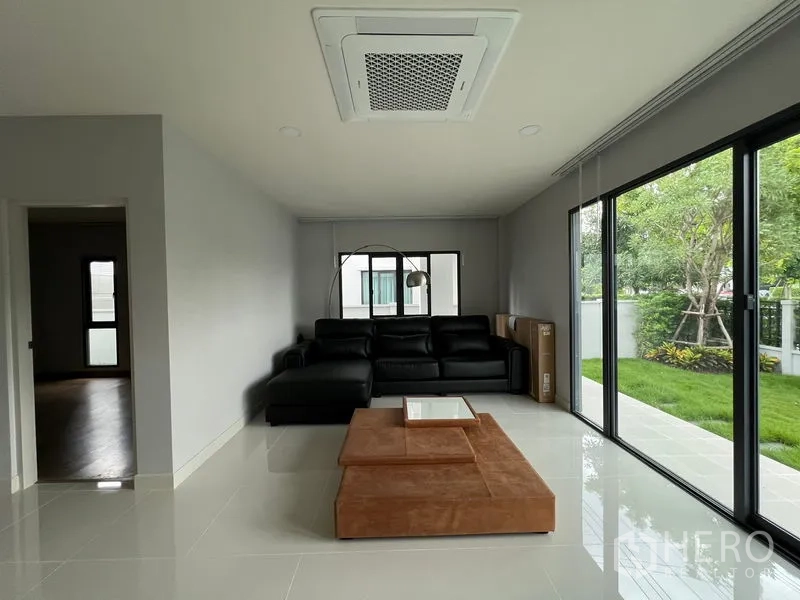 Detached House for rent or sale in Bang Phli, Samut Prakan - Ground-floor living room with black leather sofa and wide glass walls facing the garden.