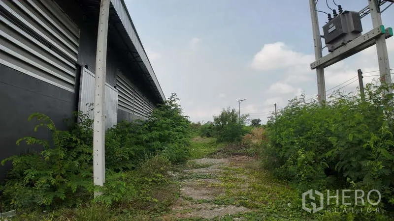 Warehouse for rent in Chachoengsao - Narrow side path with greenery, exterior wall and on‑site power transformer.