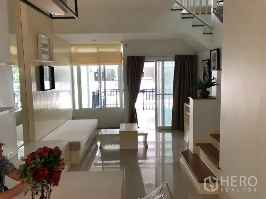 联排别墅 出租在Prawet, Bangkok - 明亮客厅，亮面地砖，内置长椅，落地玻璃门与楼梯。