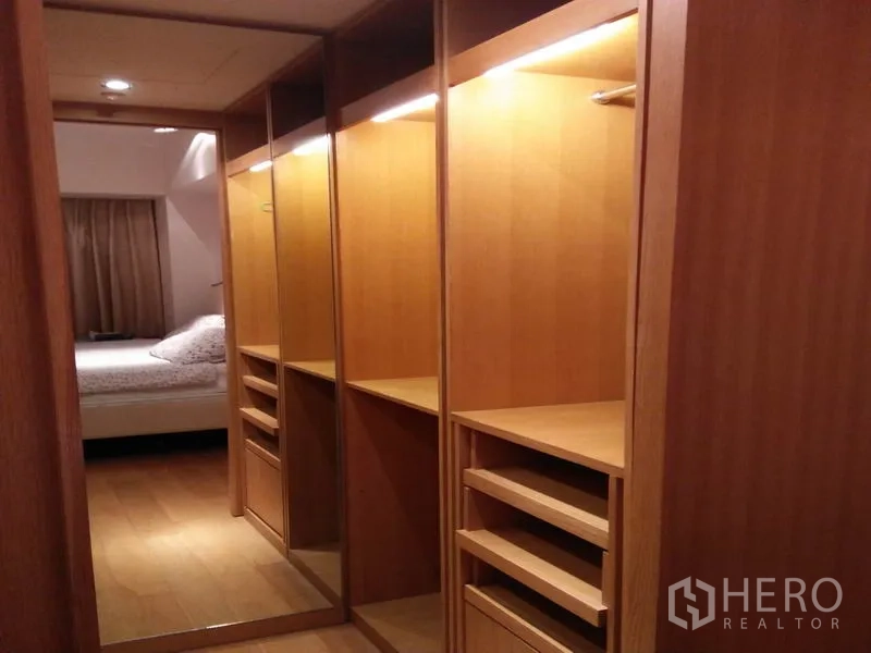 Condominium for rent in Sathon, Bangkok - Walk-in wardrobe with illuminated wooden cabinetry and mirror leading to the bedroom.