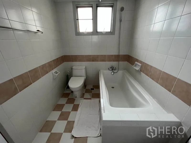 公寓 出租在Watthana, Bangkok - 浴室铺白色瓷砖和米色腰线，设浴缸、手持花洒与座厕。