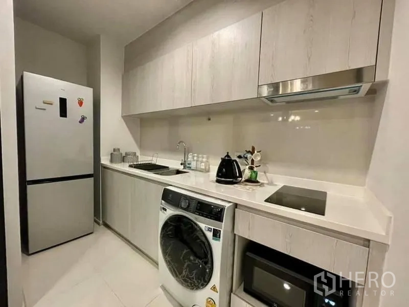 Condominium for rent in Pathum Wan, Bangkok - Modern galley kitchen with white cabinetry, cooktop, fridge and washer-dryer.