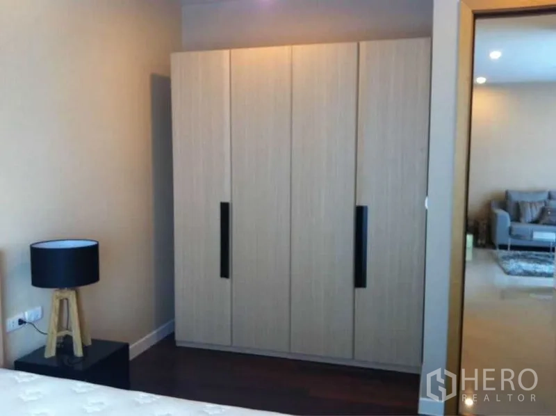 公寓 出售在Ratchathewi, Bangkok - 卧室一角设木纹衣柜与床头灯，门外连接客厅。