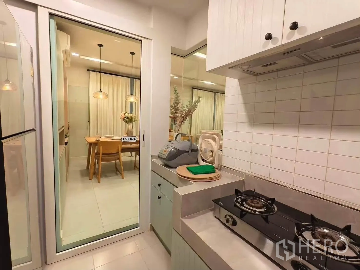 独栋房屋 for rent in Bang Phli, Samut Prakan - 封闭式厨房配燃气灶与白色墙砖，玻璃滑门通往餐区。
