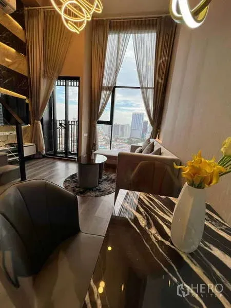 Condominium for sale in Chatuchak, Bangkok - Loft-style condo living and dining area with marble table, floor-to-ceiling windows and a balcony with city views near BTS Phahon Yothin 24.