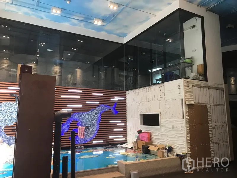 零售空间 出租在Khlong Toei, Bangkok - 挑高零售空间，马赛克鲸鱼主题墙与浅水展示池，旁有玻璃房。