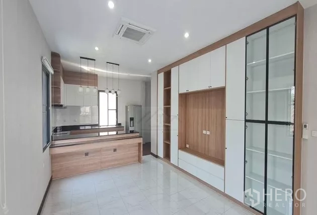 Home Office for rent in Watthana, Bangkok - Open‑plan dining and kitchen space with an island counter, ceiling downlights and built‑in storage with glass display cabinets.