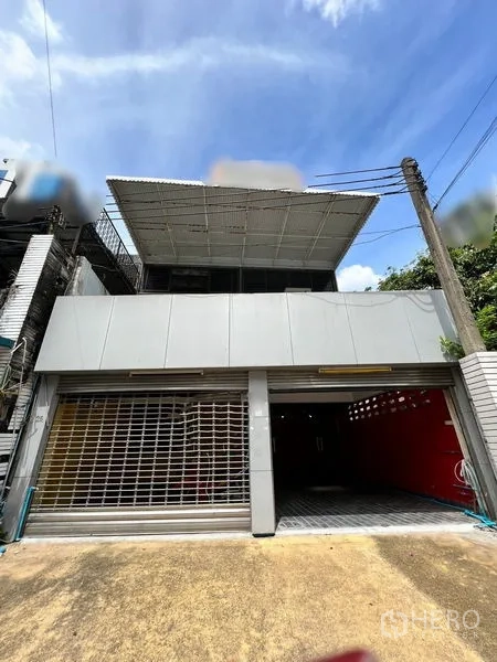 Townhouse for rent in Khlong Toei, Bangkok - Two-storey townhouse facade with wide roller doors and metal awning.