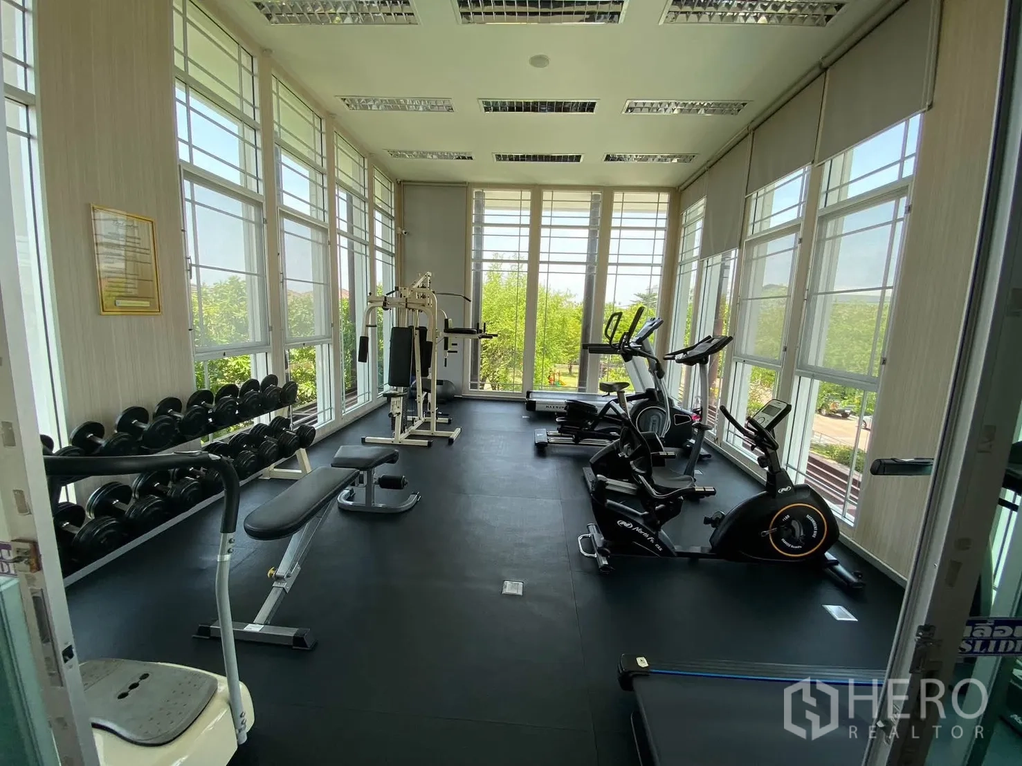 Detached House for rent in Mueang Samut Prakan, Samut Prakan - Bright fitness room with cardio machines, free weights, and tall windows.