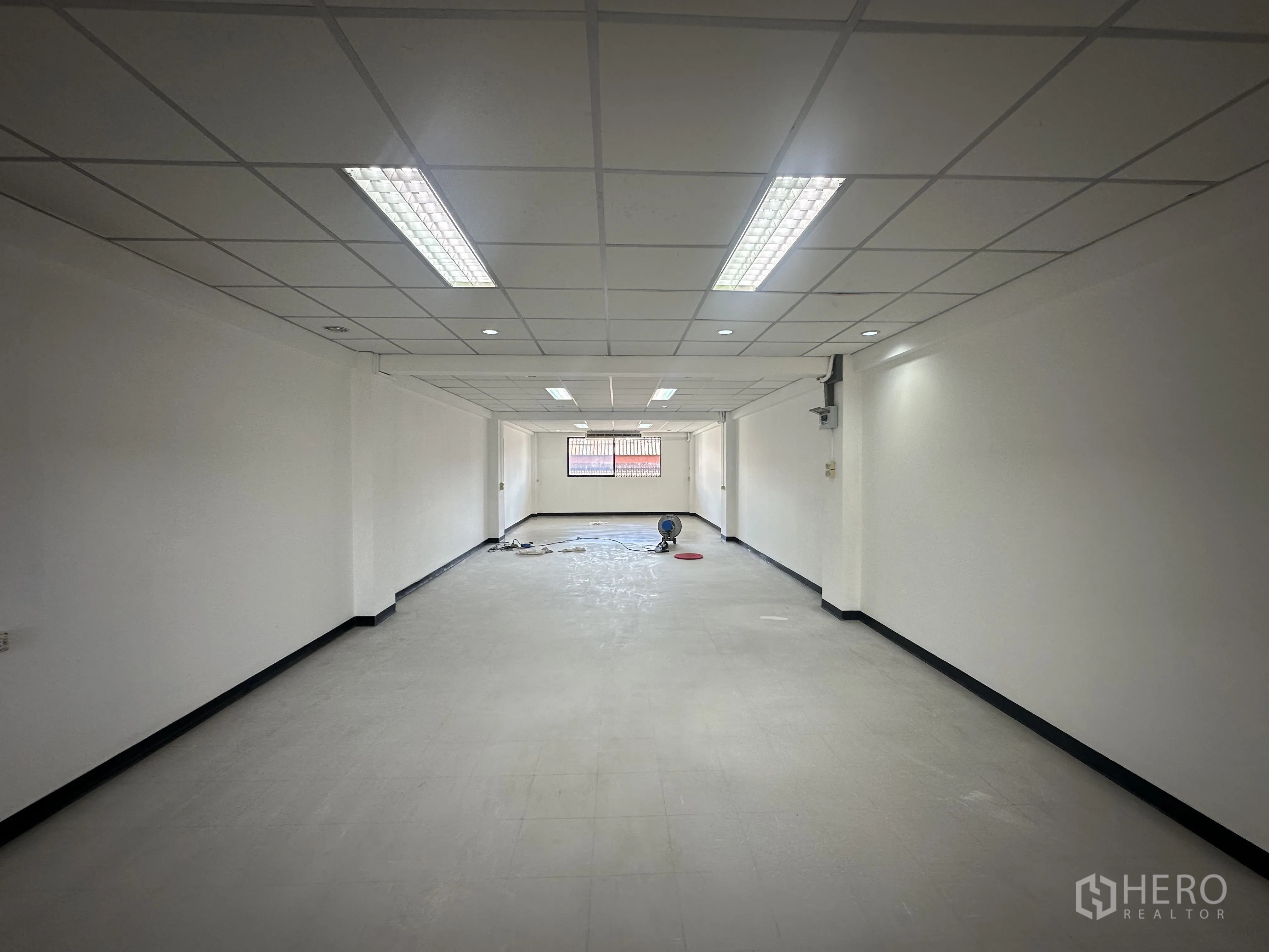 Office Space for rent in Watthana, Bangkok - Long rectangular office space with recessed and fluorescent lighting, white walls and a window at the far end.