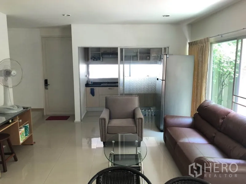 ทาวน์เฮาส์ ให้เช่าหรือขายในSuan Luang, Bangkok - โถงรับแขกแบบโอเพ่นพร้อมโซฟาและโต๊ะกลางกระจก มองไปยังครัวกั้นกระจกและตู้เย็น