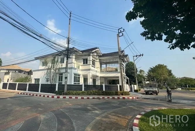 Detached House for sale in Pak Kret, Nonthaburi - Street-side angle of a modern white two-storey house with perimeter fence on a corner.