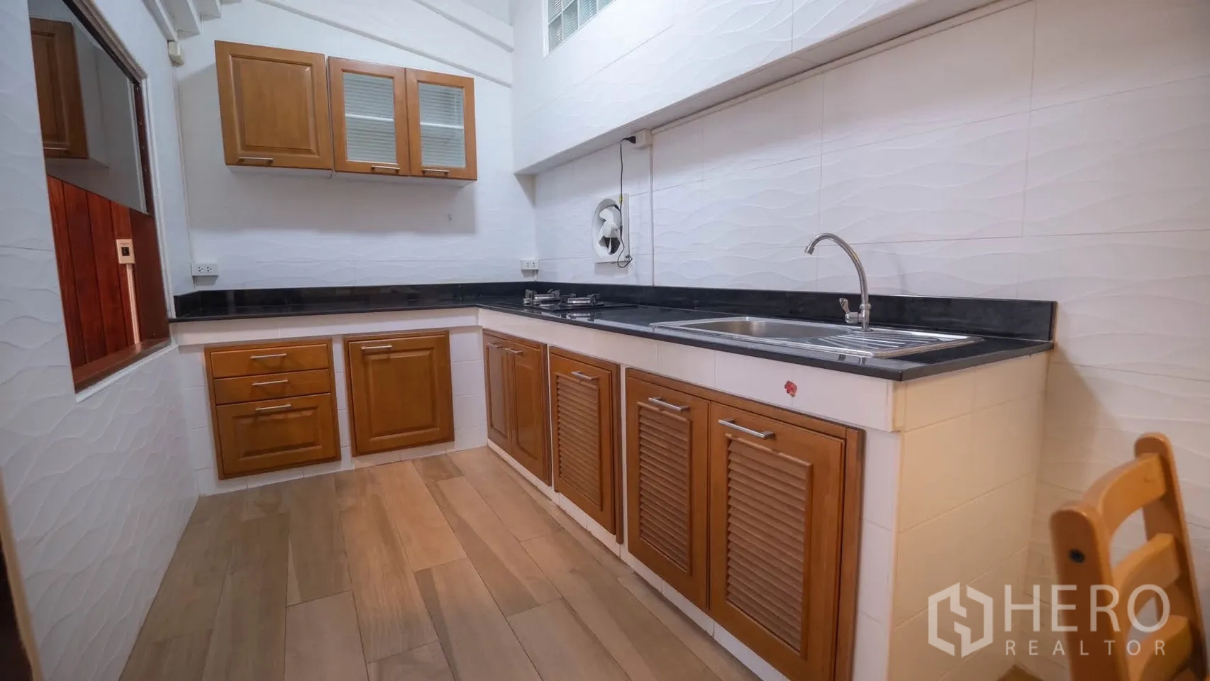 Townhouse for rent in Watthana, Bangkok - Practical kitchen with wooden cabinets, black countertops, double sink, and gas hobs.